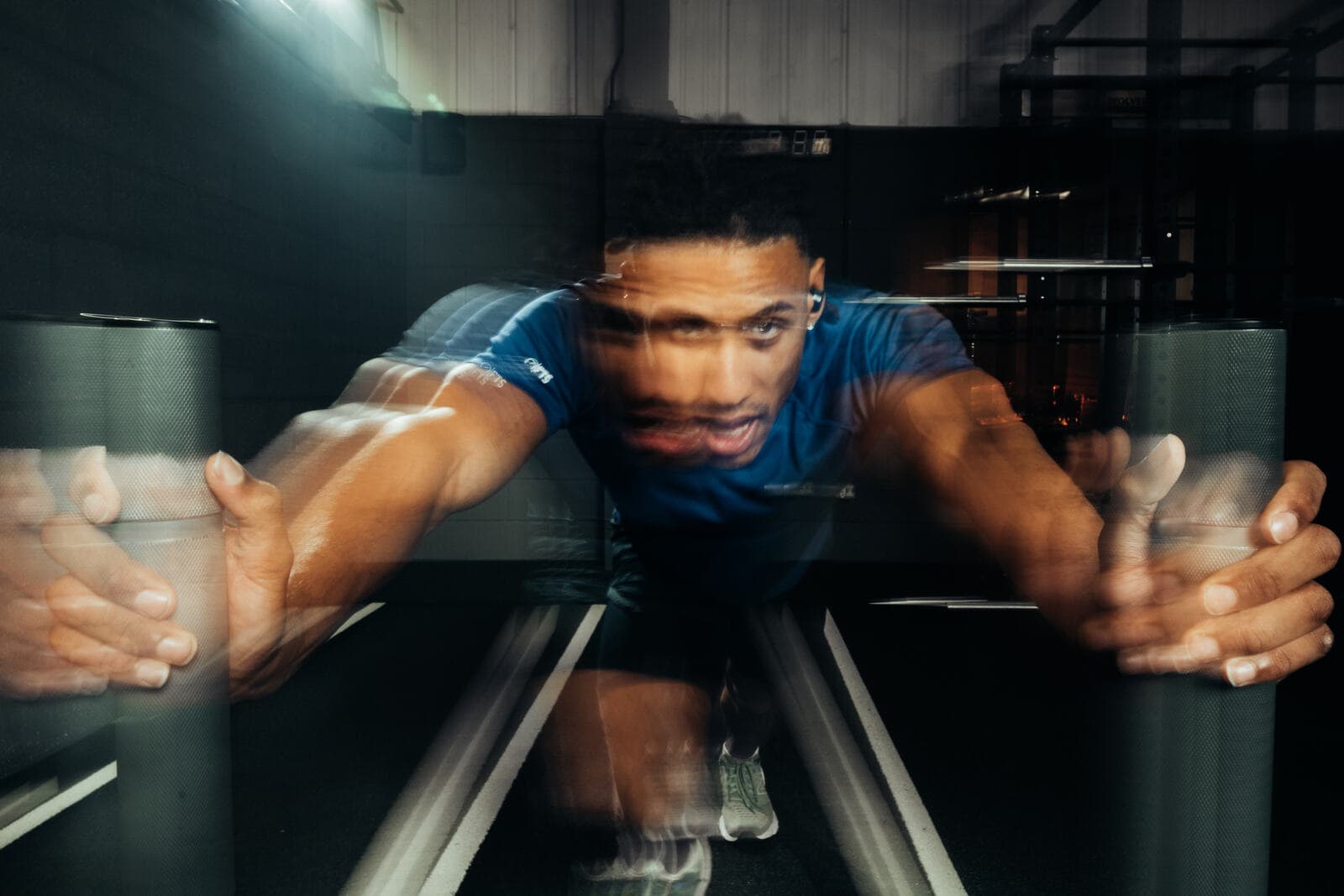 Athlete driving a heavy sled push wearing black Tzuka TZ7 Ultra earbuds